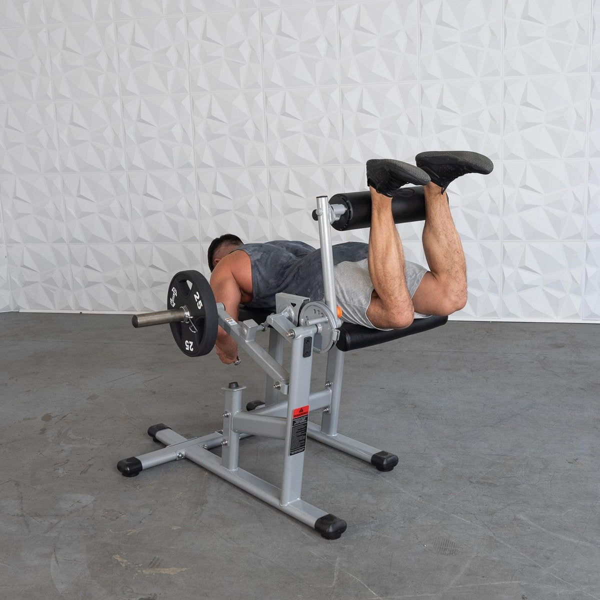 Man performing leg curl on a compact gym machine with a barbell nearby.