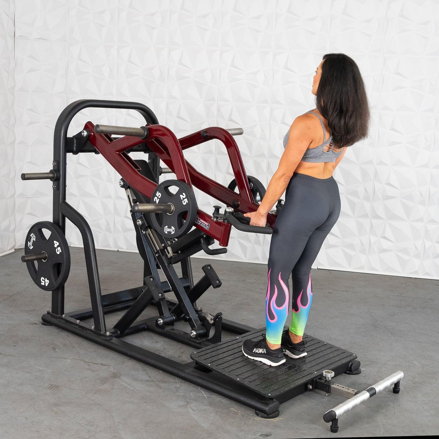 Woman using red Hack Squat machine with colorful leggings.