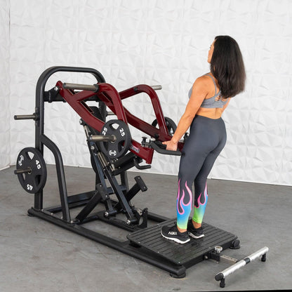 Woman using red Hack Squat machine with colorful leggings.