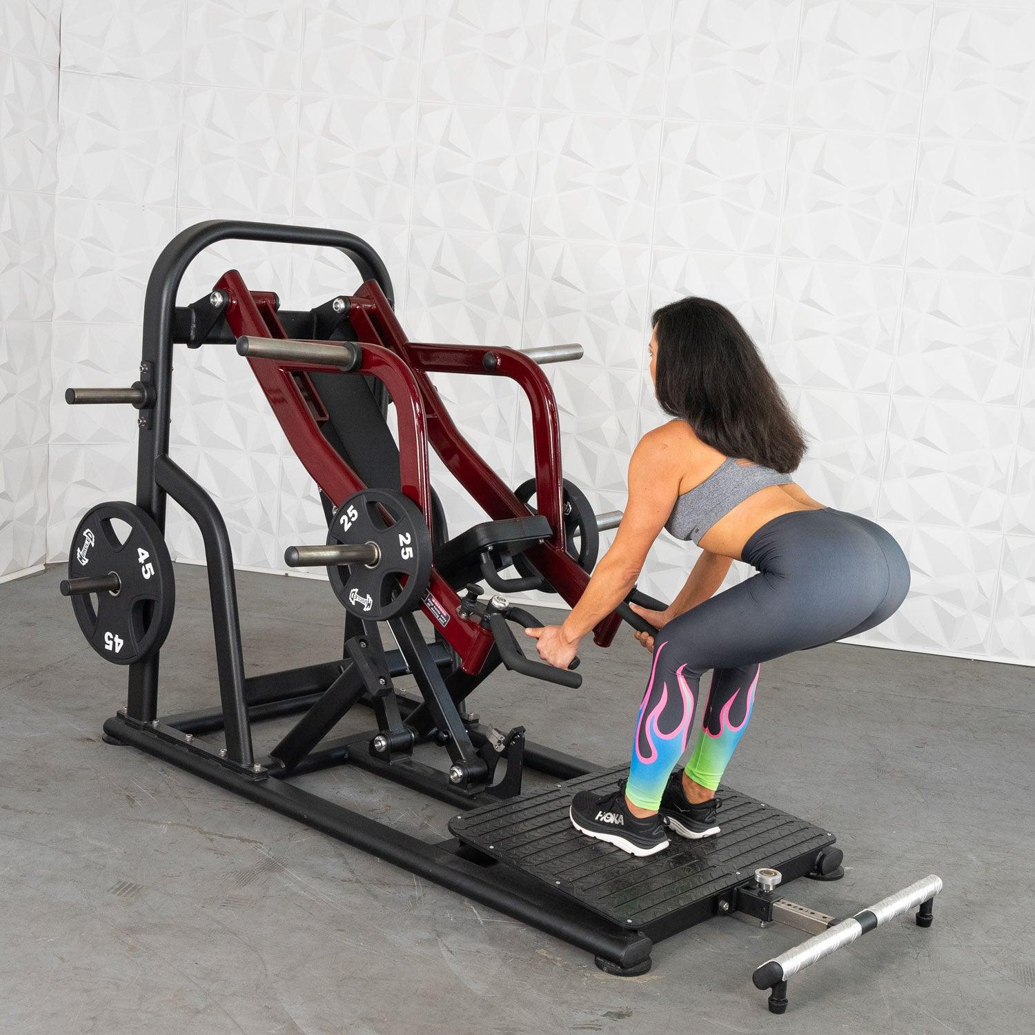 Woman using a squat machine with red handles in colorful leggings.