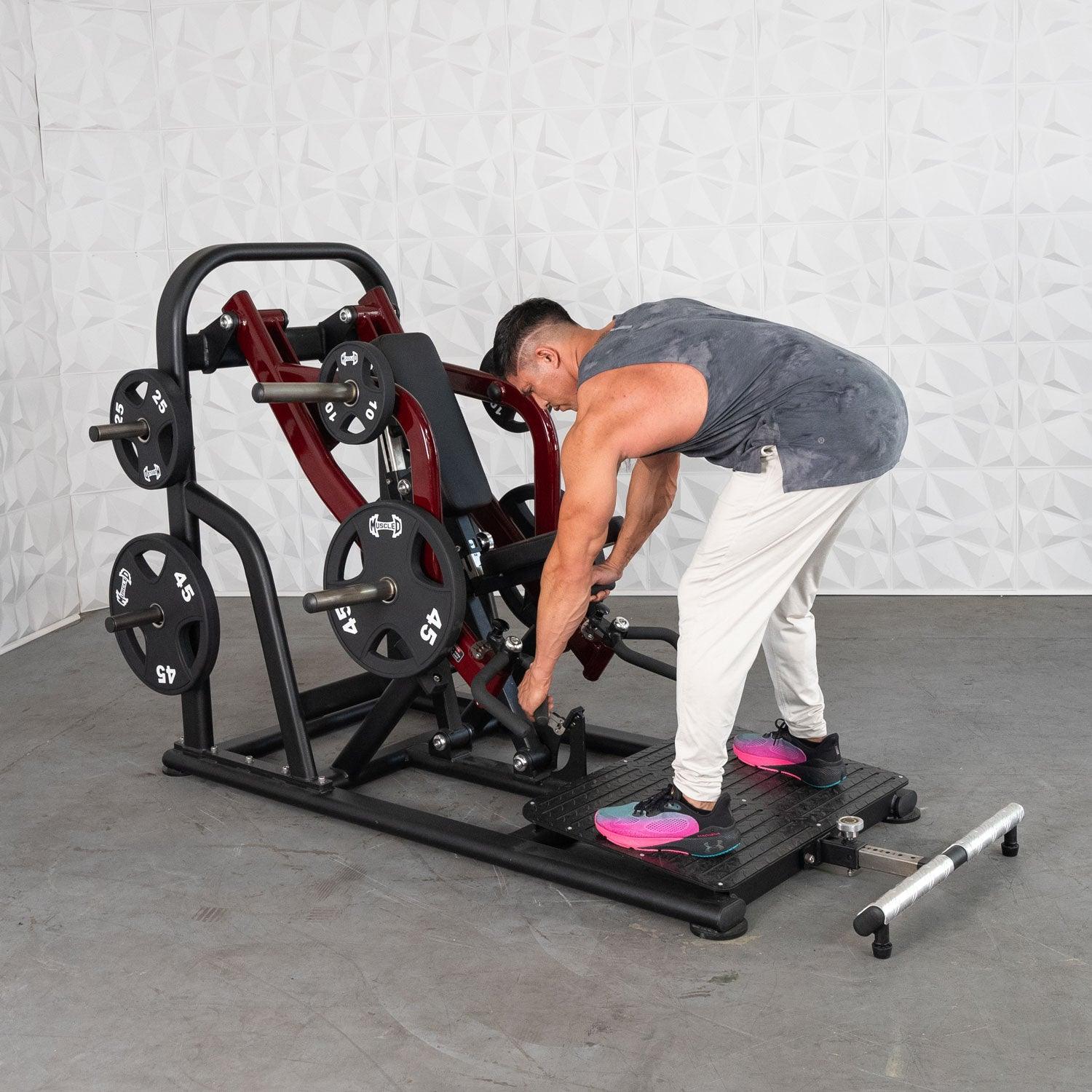 Man adjusting weights on a red leg press machine in a gym.