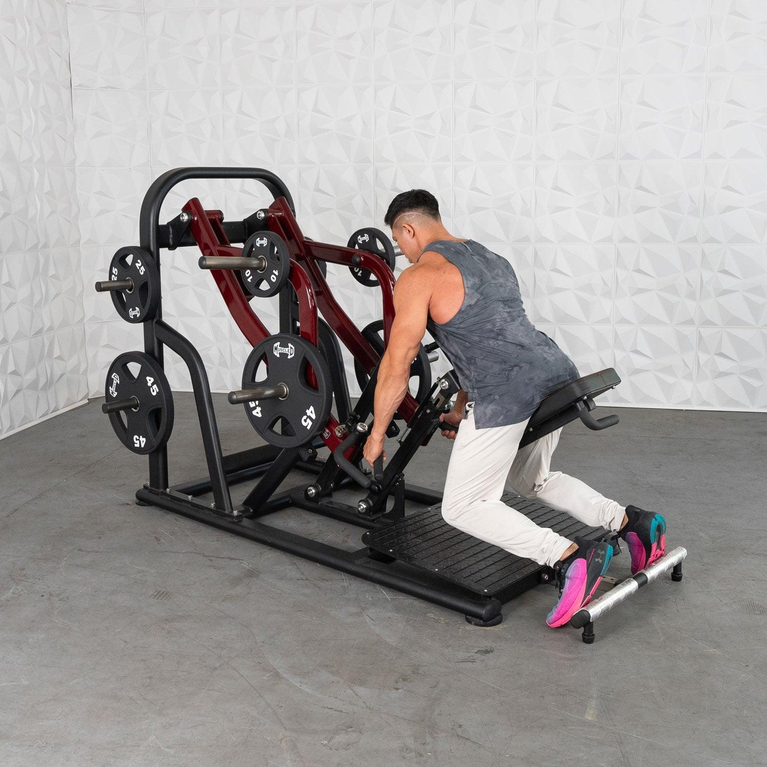 Man using a plate-loaded row machine in a gym, wearing a gray tank top and colorful sneakers.