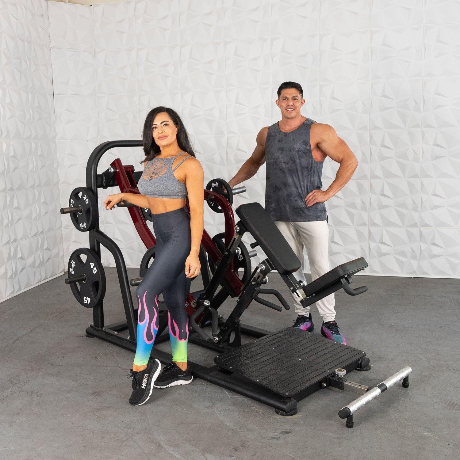 Two people with a leg press machine, one wearing colorful leggings and sneakers, in a gym setting.