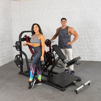 Two people with a leg press machine, one wearing colorful leggings and sneakers, in a gym setting.