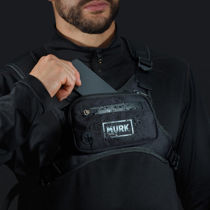 Person holding a black tactical vest with 'MVRK' logo on a dark background