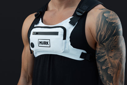 Man wearing a white chest rig with MVRK logo and a tattooed arm.