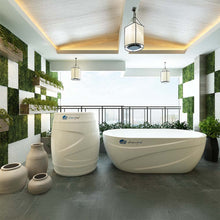 A modern outdoor space featuring the Dreampod Cold Plunge Barrel alongside a sleek white soaking tub, surrounded by greenery and decorative planters, with stylish lighting fixtures above.