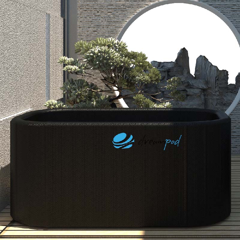 Dreampod Cold Plunge Flex, a sleek black plunge tub, situated on a wooden deck with a plant nearby and a circular window showcasing rocky terrain in the background.