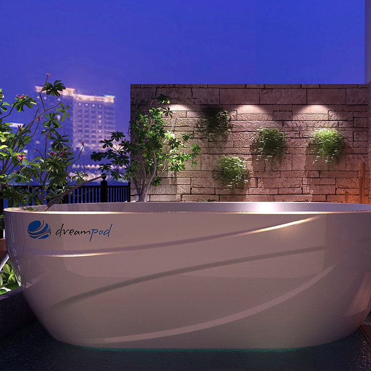 Dreampod Commercial Cold Plunge, a sleek white tub surrounded by greenery and illuminated by soft lights, set against a nighttime city backdrop.