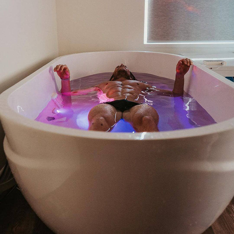 A person relaxing in a Dreampod Commercial Cold Plunge, submerged in water with colorful lighting effects, showcasing a modern, sleek design.