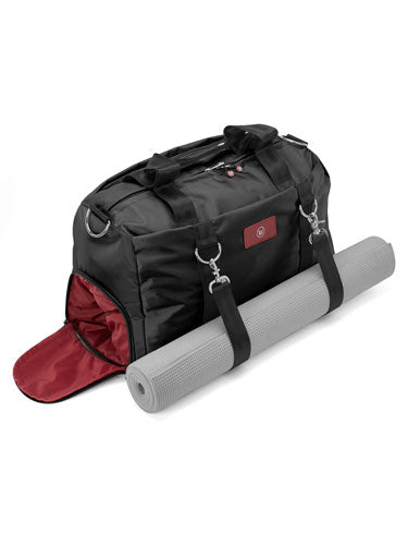 Black duffel bag with red interior and a rolled gray yoga mat beside it.