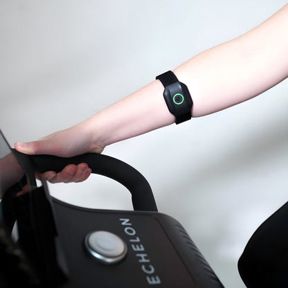 A close-up of a hand gripping the handle of an exercise machine, wearing an Echelon Beat Advanced Armband Heart Rate Monitor on the wrist.