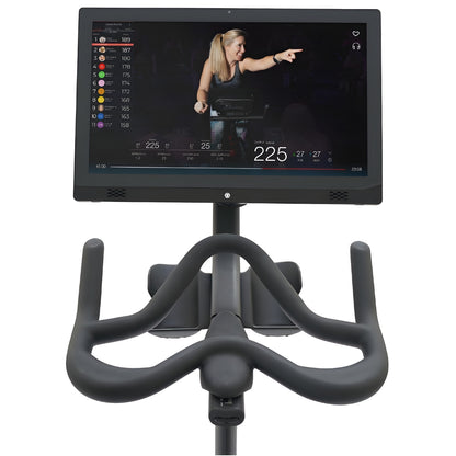 Close-up view of the Echelon EX-7s Smart Connect Bike, featuring a large screen displaying workout metrics and an instructor pointing, with bike handlebars visible in the foreground.