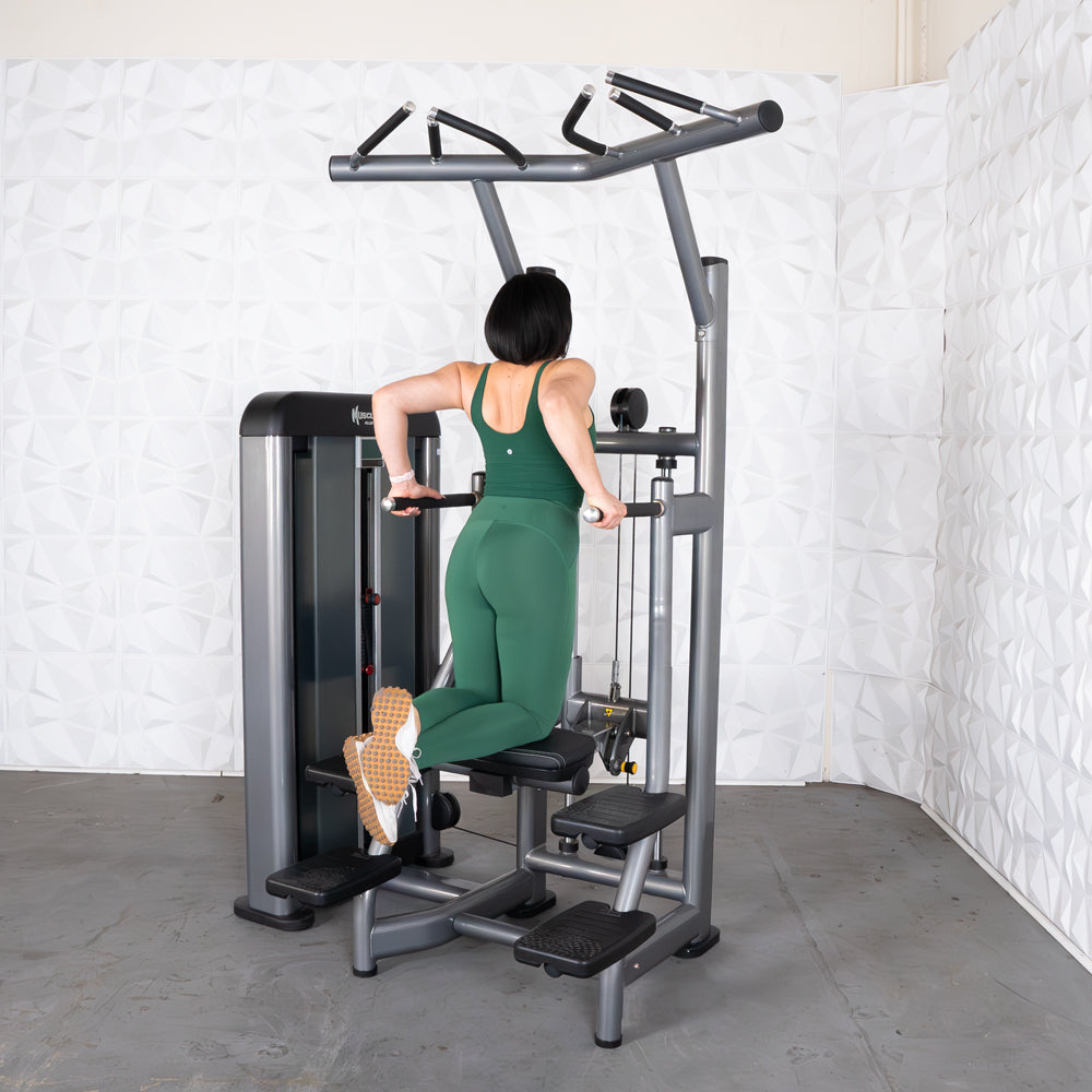 Woman in green workout outfit using dip machine in gym.