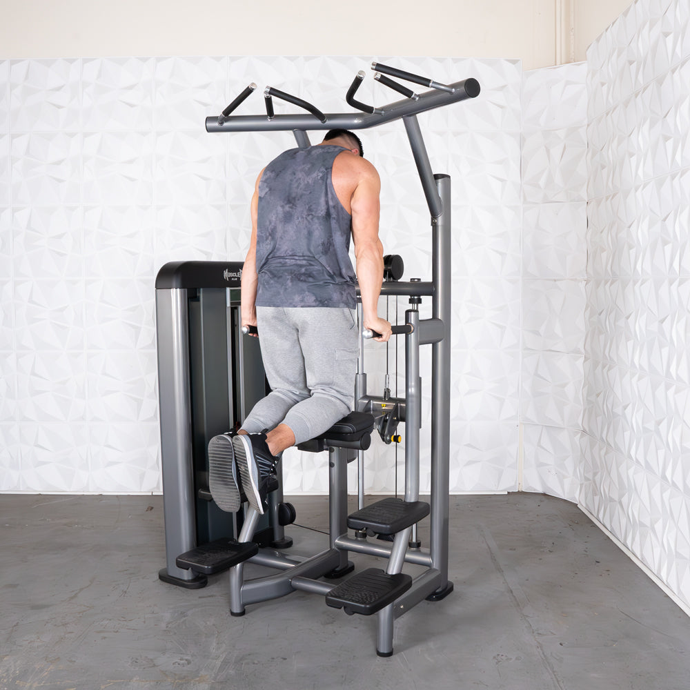 Man using a dip assist machine in a gym, wearing gray sweatpants and a dark tank top.