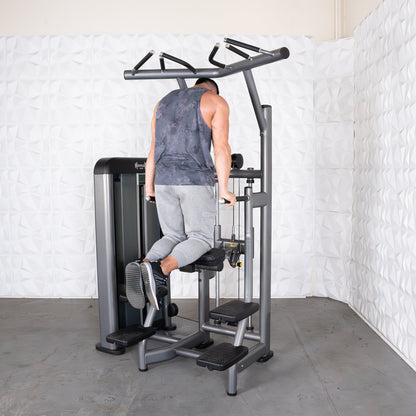 Man using a dip assist machine in a gym, wearing gray sweatpants and a dark tank top.