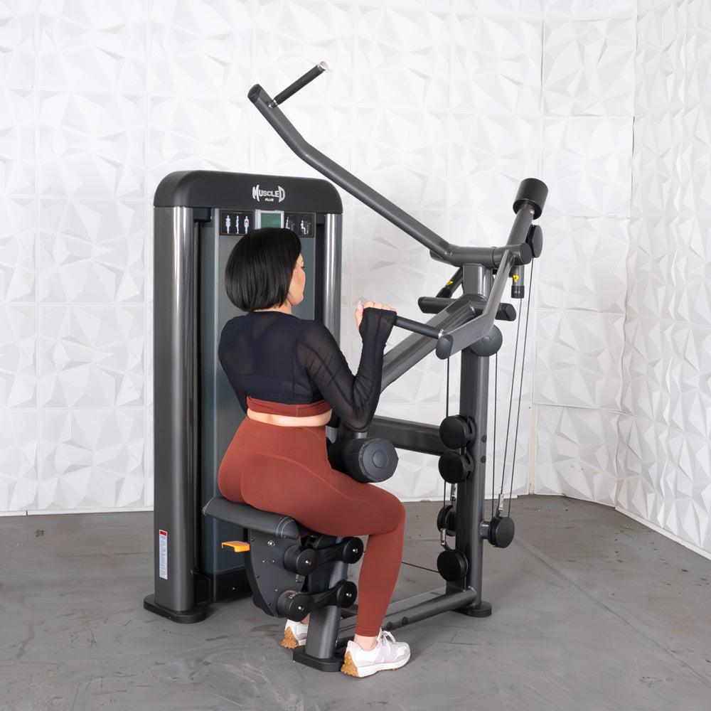 Woman using Muscle D fitness machine in black top and brown leggings.