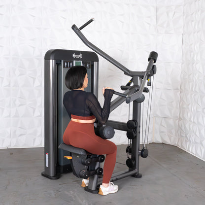 Woman using Muscle D fitness machine in black top and brown leggings.