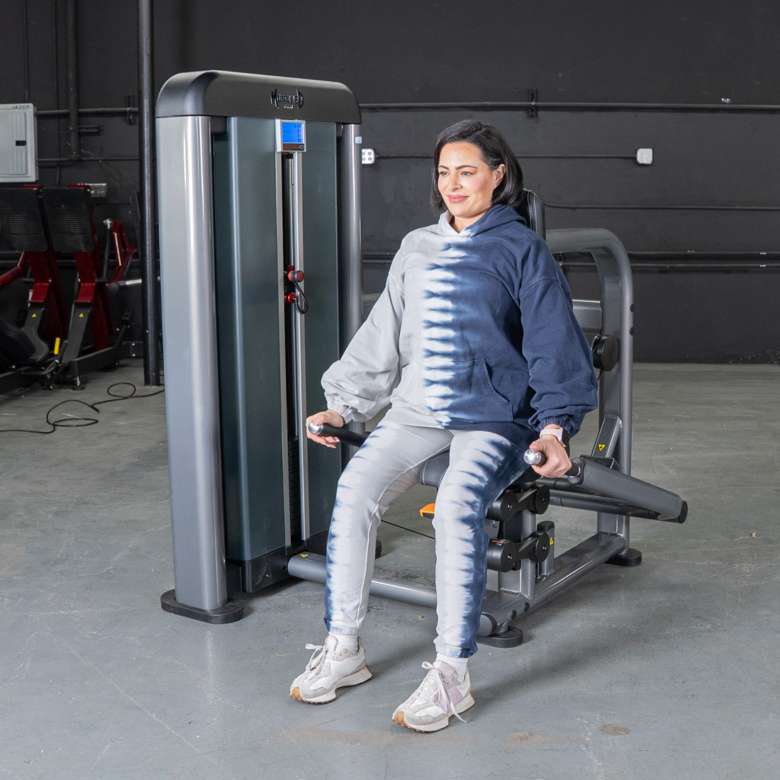 Woman seated on Elite Plus Triceps Press machine in gym.