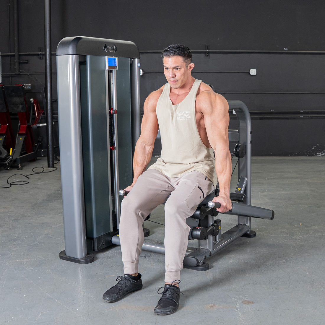 Muscular man seated on a triceps press machine at the gym.