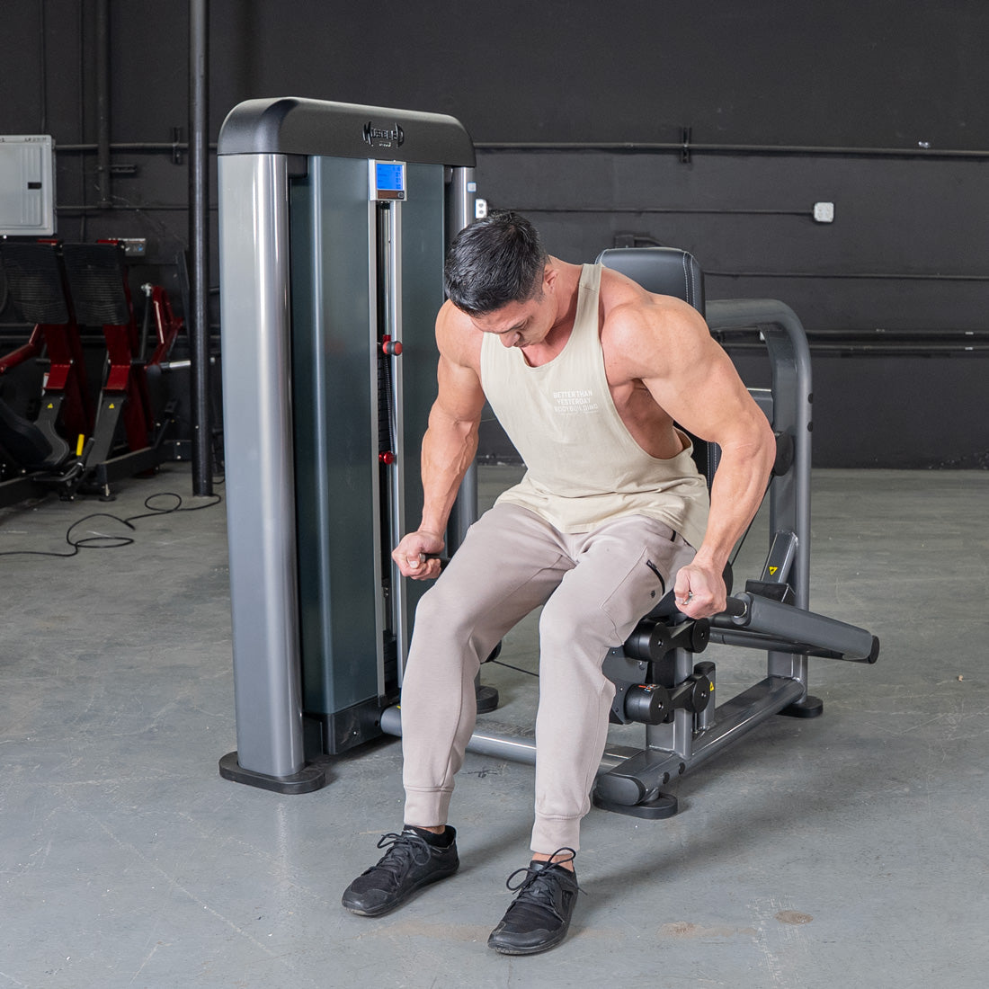 Muscular man in a tank top using a triceps press machine at the gym.