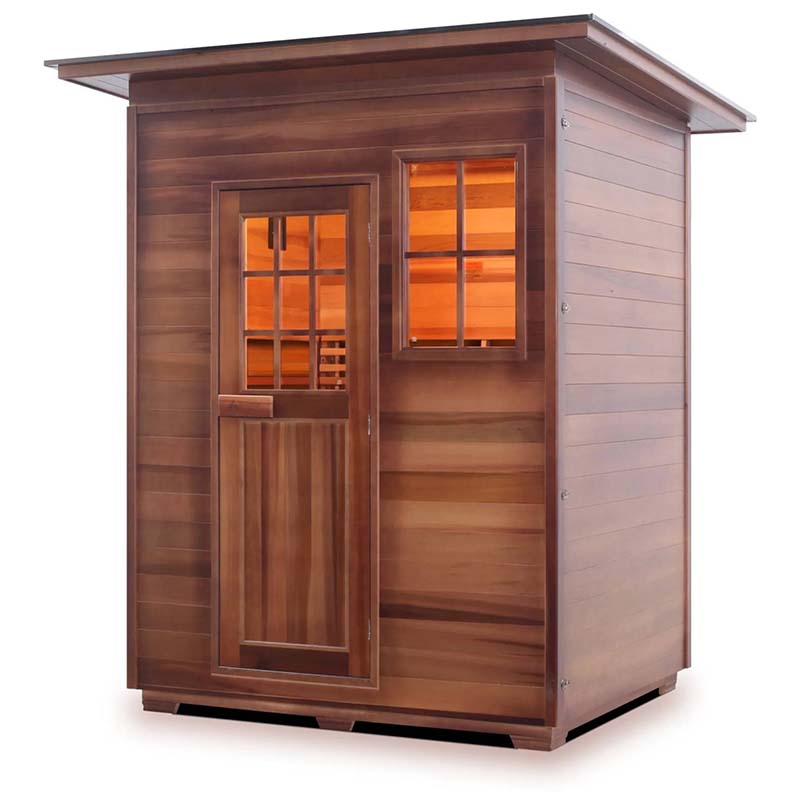 Outdoor cedar infrared sauna with glass door and window, warm glow inside.