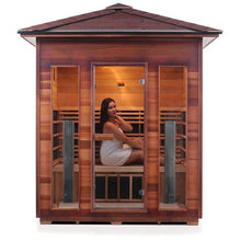 Woman relaxing in a wooden outdoor sauna cabin with large glass doors.
