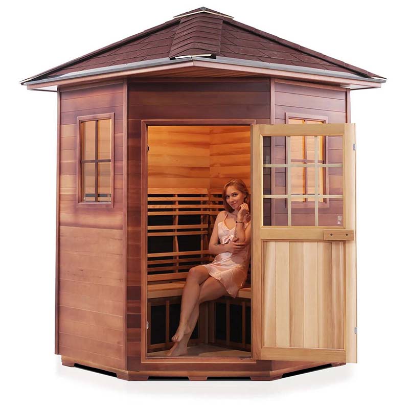 Cedar sauna cabin with woman relaxing inside, featuring glass windows and wooden exterior.