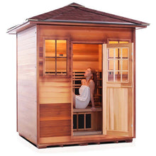 Outdoor cedar sauna with a woman relaxing inside, showcasing its wooden design and glass door.