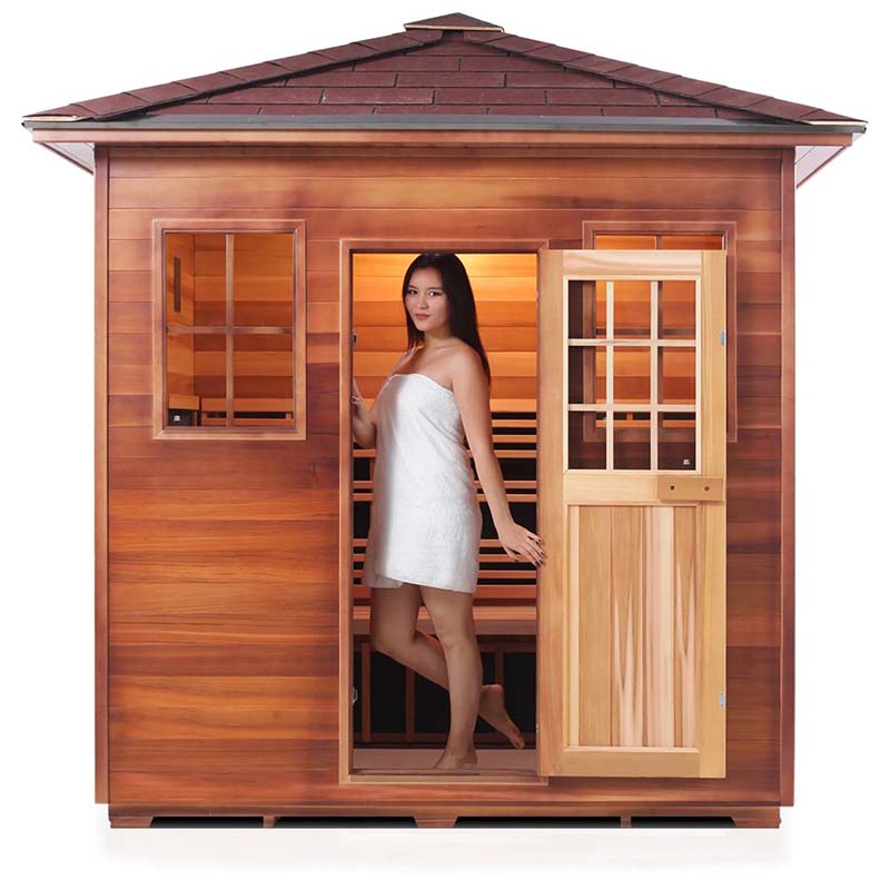 Woman in white towel standing in wooden outdoor sauna with open door.
