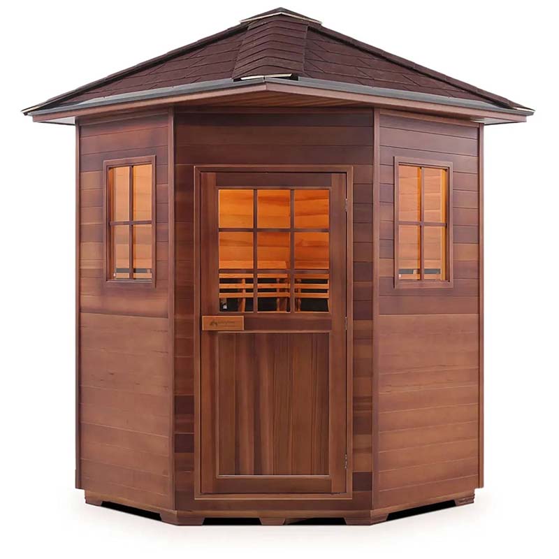 Red cedar outdoor sauna with shingled roof and glass windows, emitting a warm glow.