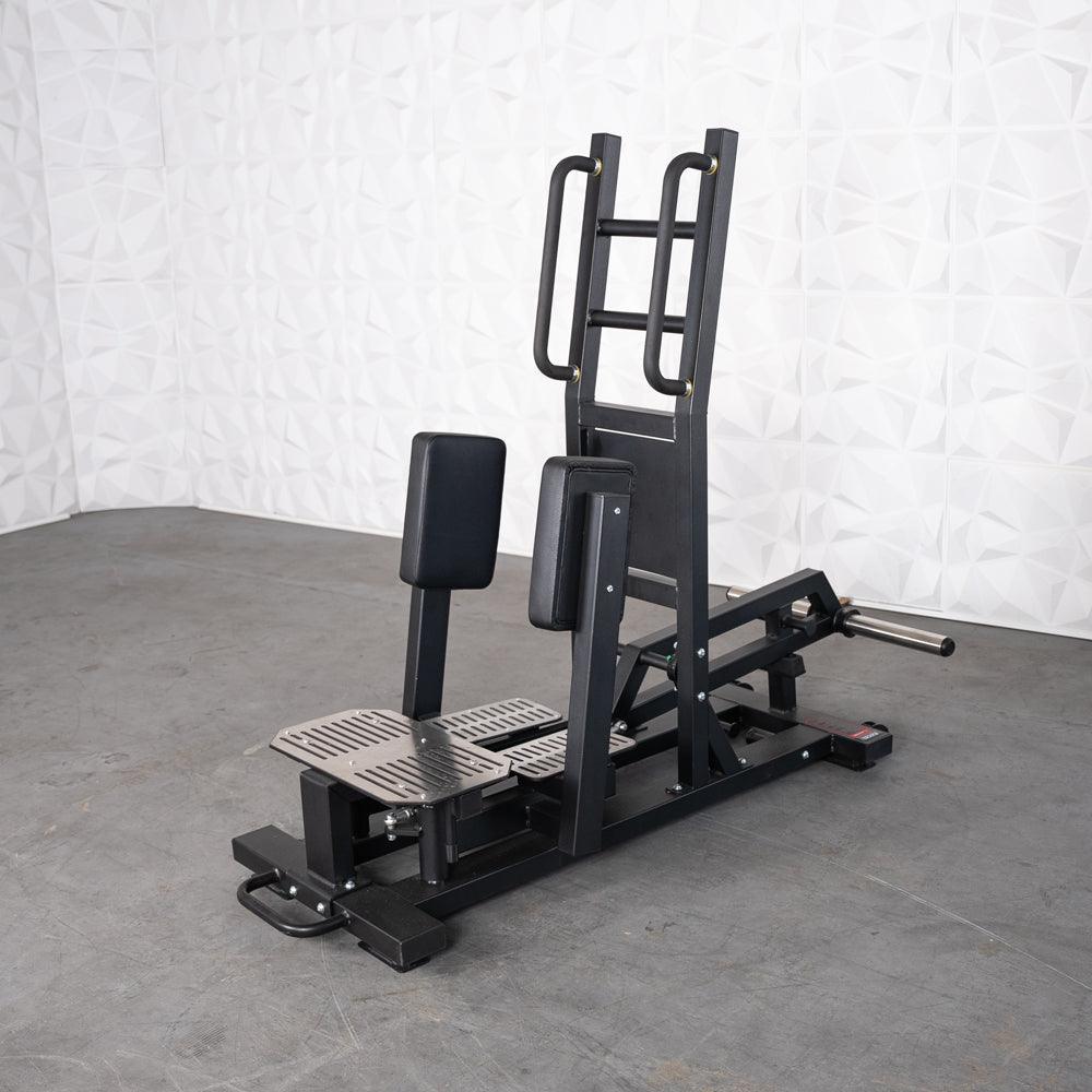 Standing hip thrust machine with pads and grip handles.