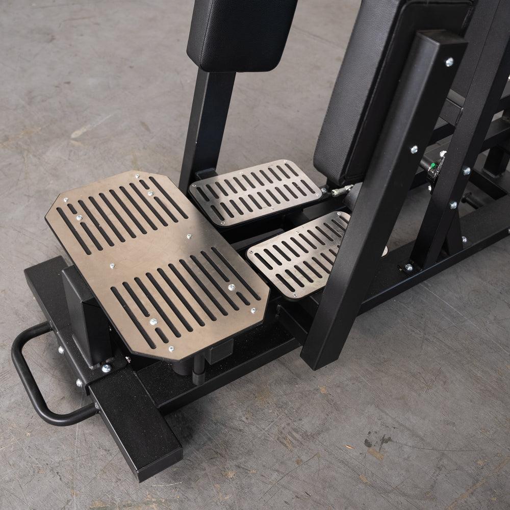 Close-up of metal foot pedals on a standing hip thrust machine.