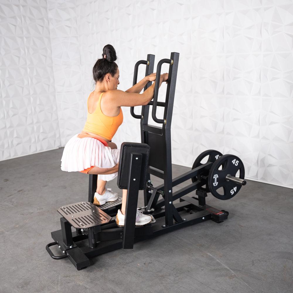 Woman using Excel Standing Hip Thrust machine in gym.