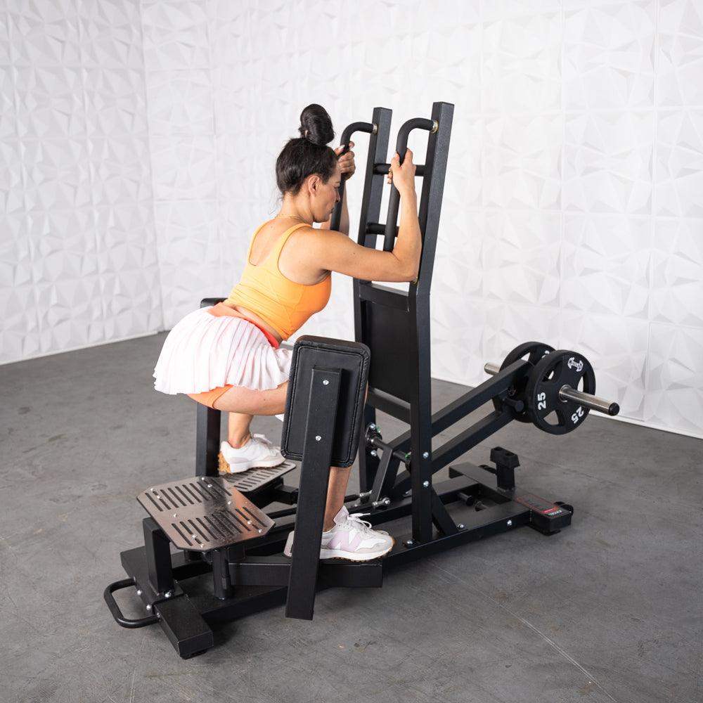 Woman performing hip thrust on a plate-loaded machine in gym.
