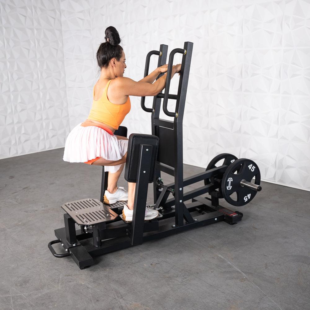 Woman using a standing hip thrust machine in a gym.
