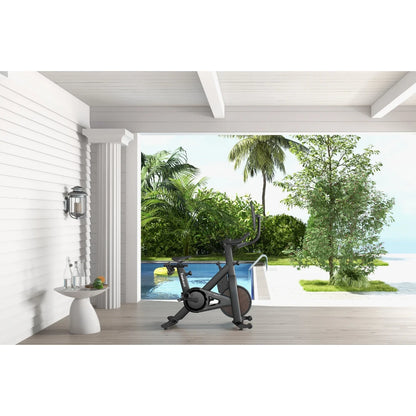 Indoor exercise bike by a poolside with lush greenery and ocean view.