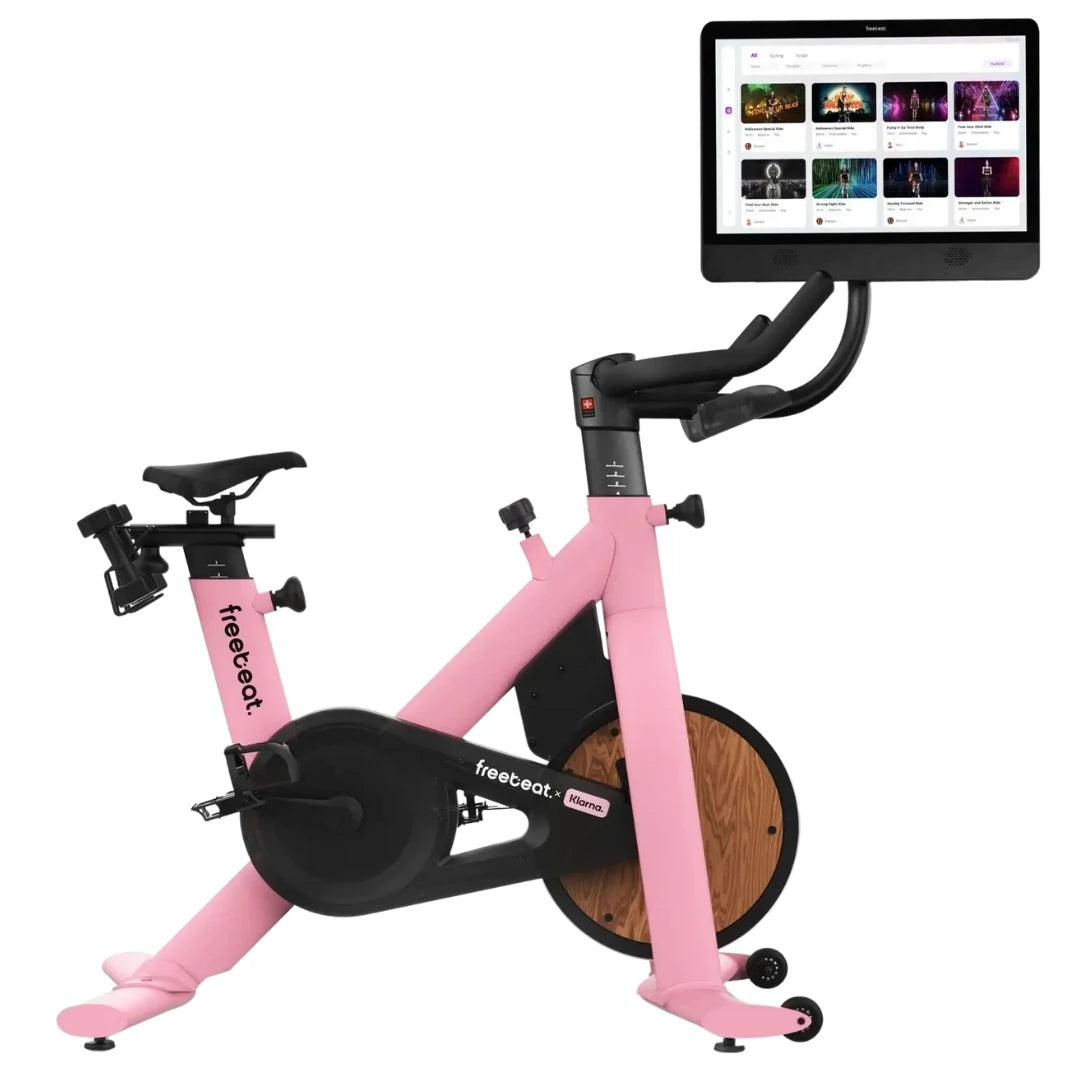 Freebeat Lit Stationary Exercise Bike in pink with a digital display screen showing various workout options.