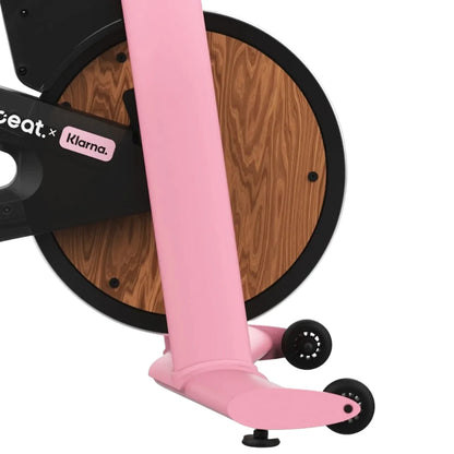 Close-up view of the Freebeat Lit Stationary Exercise Bike, showcasing its pink frame and wooden design on the flywheel.