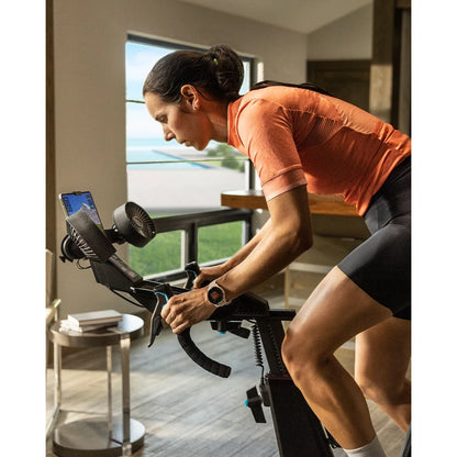 Cyclist in orange jersey using indoor training bike near window, focused on workout.