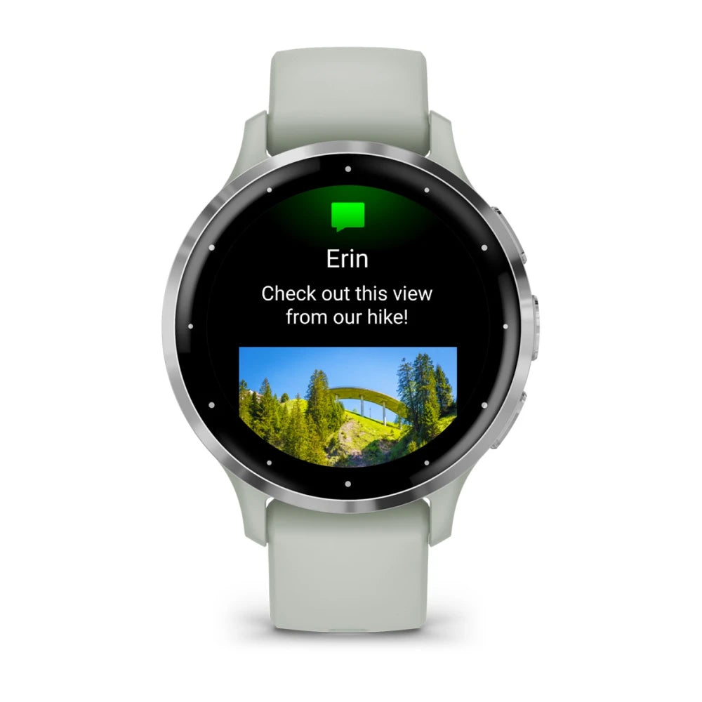 A smartwatch with a green strap displaying a message from Erin that says, Check out this view from our hike! along with a small image of a scenic landscape featuring a bridge and trees.