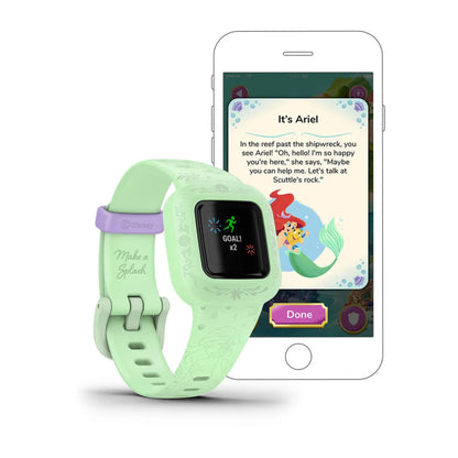 Garmin vivofit jr. 3 fitness tracker in green with a screen displaying a goal, next to a smartphone showing a Disney-themed interactive activity featuring Ariel.