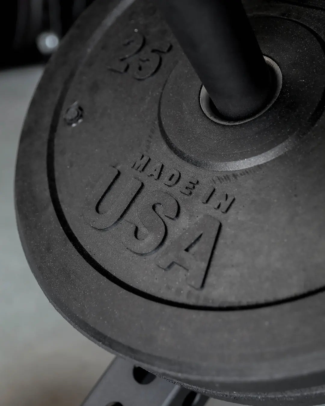 Close-up of black rubber bumper plate showing embossed weight markings and textured surface with curved edge design.