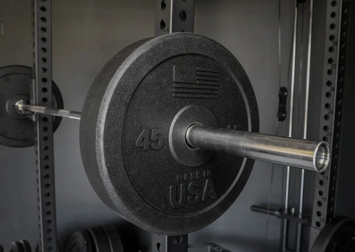 45-pound black bumper plate with textured rubber finish mounted on chrome barbell inside power rack with perforated steel uprights.
