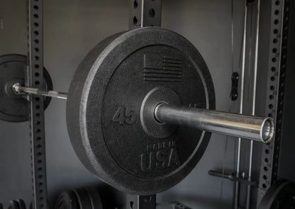 45-pound black bumper plate with textured rubber finish mounted on chrome barbell inside power rack with perforated steel uprights.