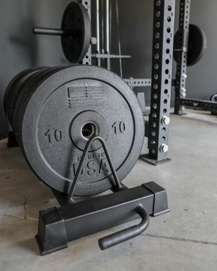 Gray bumper plate marked "10" mounted on a black base stand in a gym setting, with a power rack and additional weight plates visible in the background.