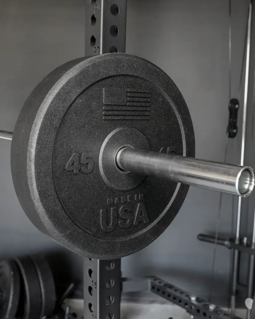 Black rubber bumper plate marked "45" loaded on a chrome barbell, mounted on a power rack with adjustment holes visible in the background.