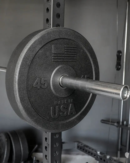 Black rubber bumper plate marked "45" loaded on a chrome barbell, mounted on a power rack with adjustment holes visible in the background.