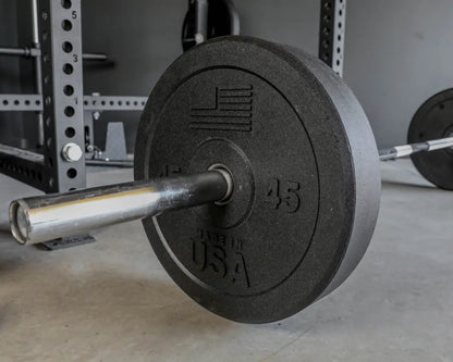 Black rubber bumper plate with "45" and "USA" markings loaded on a chrome barbell in a home gym setting with a power rack visible in the background.