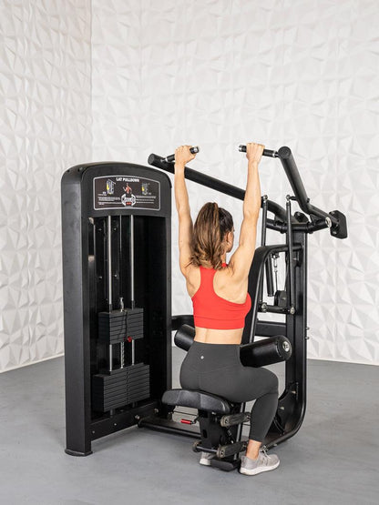 Woman using lat pulldown machine in red top and black leggings.